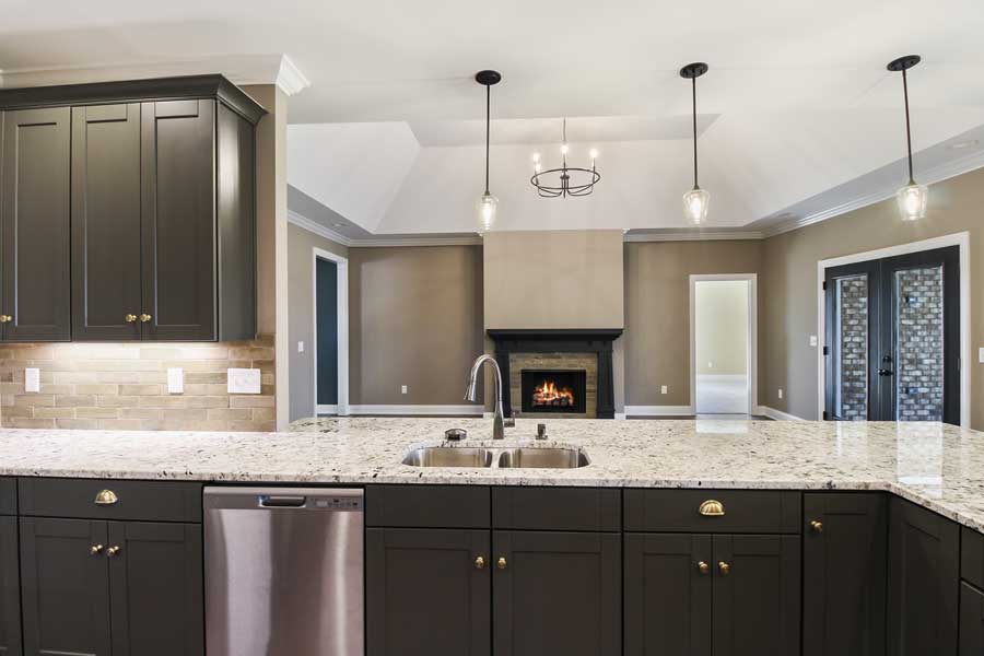 open concept kitchen and living area with granite countertops, black cabinets and a fireplace. Vaulted ceiling.