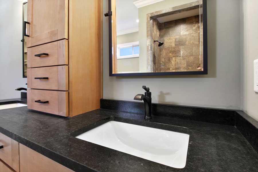 black sink and faucet with wood cabinets and a large mirror
